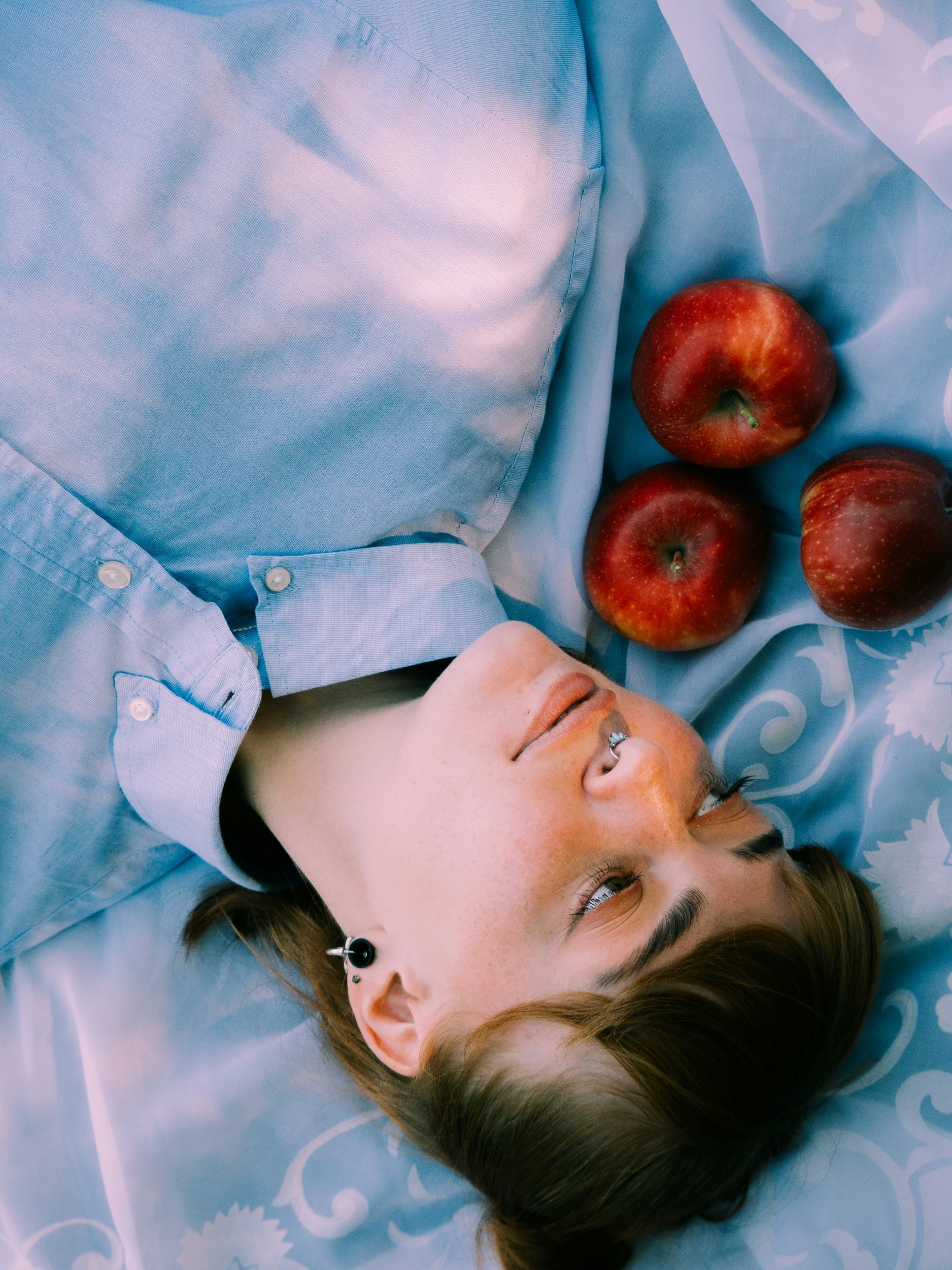 Chica recostada sobre tela azul con manzanas rojas